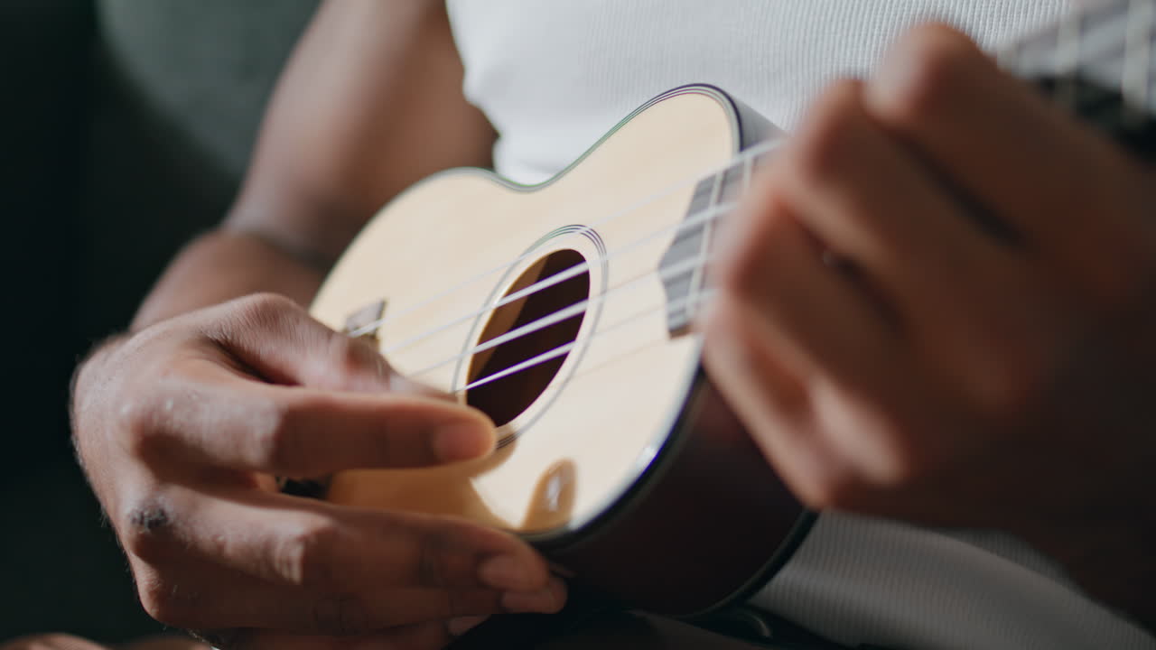 hombre manos tocando ukulele en el interior. músico desconocido tocando cuerdas en casa