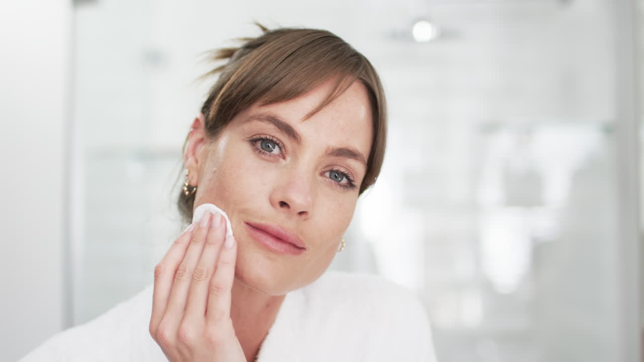 Caucasian woman with brown hair is cleansing her face with a cotton pad