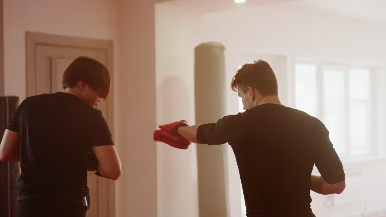 Boxer wearing black gloves trains with partner during gym workout session, showing focus, preparation, athletic stance, combat readiness, energy, determination, and intense commitment