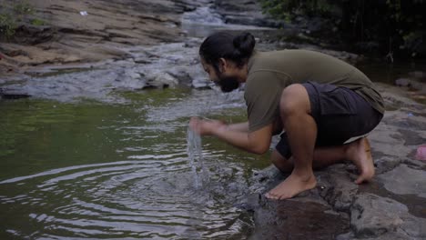 vivek bearded long hair man washing face in fresh water in jungle