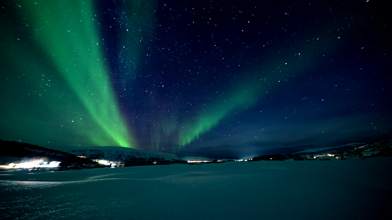 La costa invernale di Skogsfjord risplende mentre alti fasci di aurora si diffondono su terra ghiacciata e acqua scura, statico.