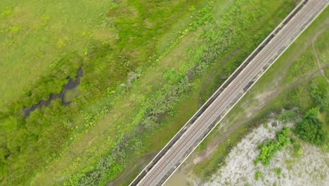 Spinning-aerial-footage-revealing-the-elevated-railway,-canals-with-water,-grassland,-Muak-Klek,-Saraburi,-Thailand