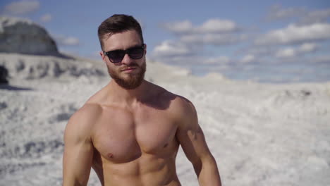 muscular sportsman outdoors. handsome shirtless man showing his arm biceps while standing on white canyon on black car background in summer day. close-up.