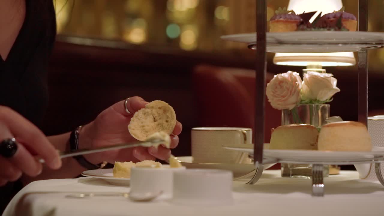 A young girl is spreading clotted cream on the half scone in slow motion. Elegant female movement while the camera is following her hands