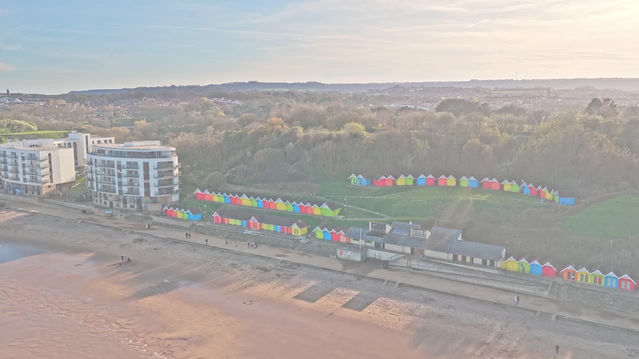 Praia de North Bay em Scarborough, North Yorkshire, Inglaterra, Reino Unido, com chalés de praia coloridos ao longo do calçadão, edifícios à beira-mar adjacentes e infraestrutura costeira, em um afastamento de drone.