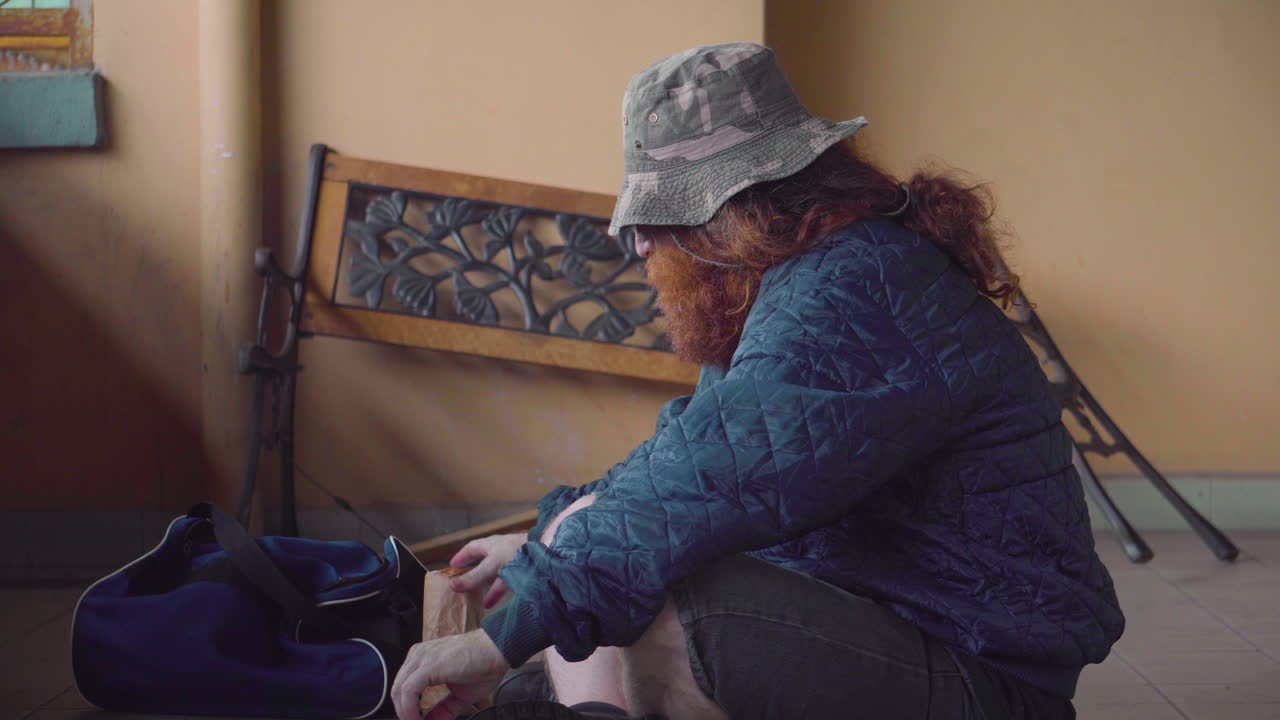 hombre sin hogar fumando cigarrillo solo al aire libre cerca de un banco roto tiro medio lata de cerveza bebiendo