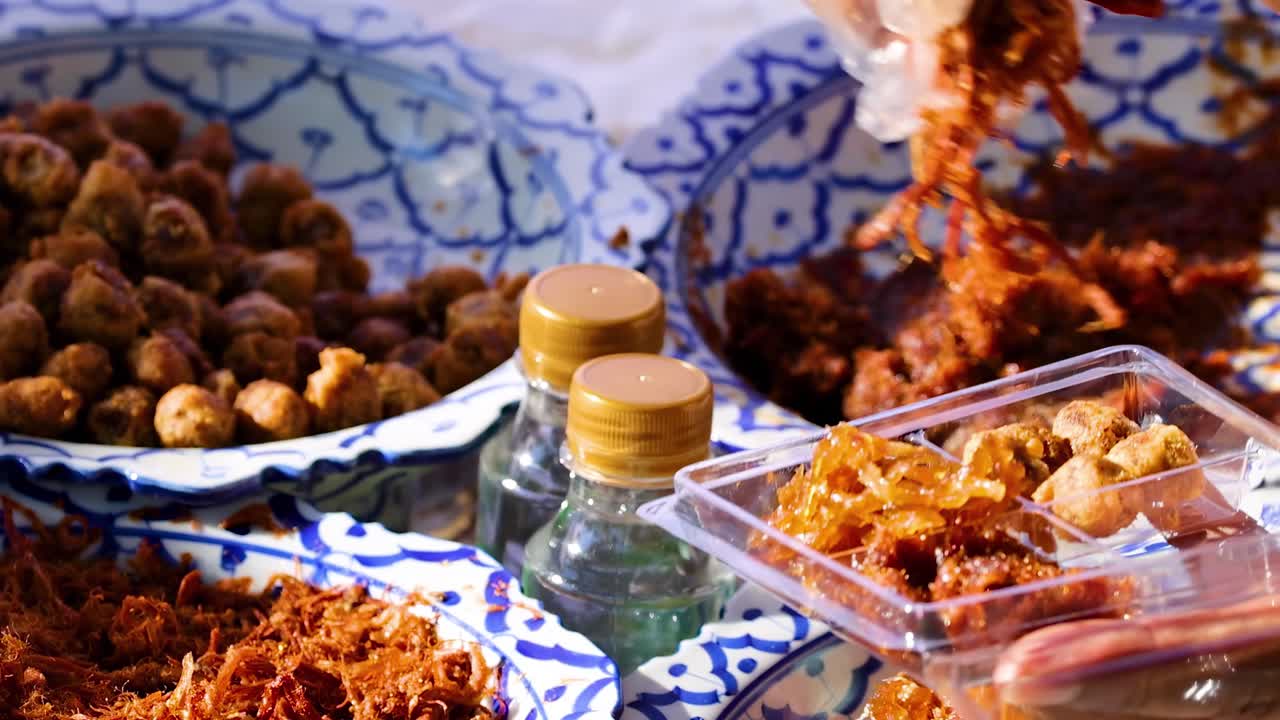 A vendor uses gloved hands to pack shredded pork into clear plastic containers at a market stall.