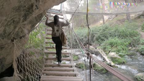 woman hiking on wooden suspension bridge in mountainous forest