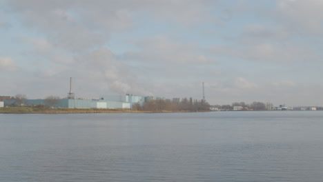 White-smoke-rising-from-industrial-building-on-river-shore---wide