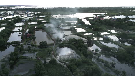 aerial view of tonlé sap wetlands with smoke rising from a small homestead among reflective ponds