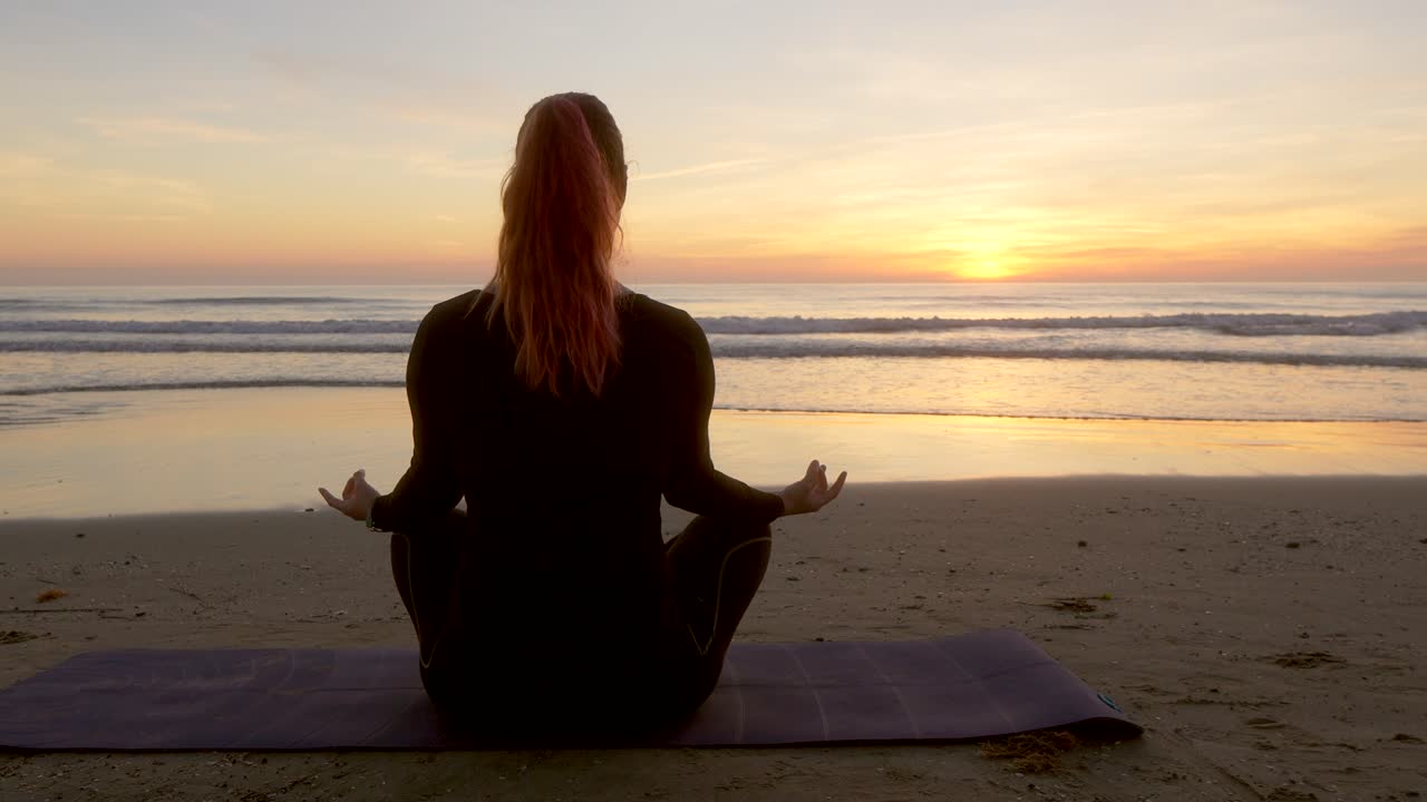 mujer meditando mientras sostiene una flor de loto mirando el mar durante el amanecer