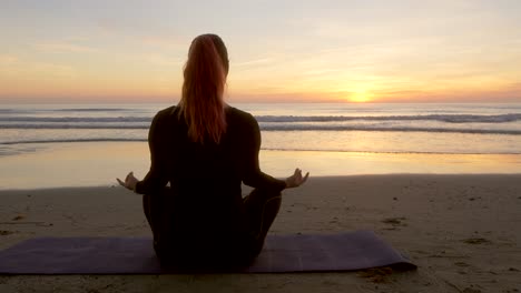 Frau-Meditiert,-Während-Sie-Eine-Lotusblume-In-Der-Hand-Hält-Und-Bei-Sonnenaufgang-Auf-Das-Meer-Blickt