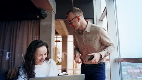 cheerful smiling people talking in the office. man stands near the woman sitting at desk. colleagues peaking and laughing. low angle view.