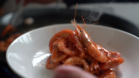 cook removing fried prawns from the heat during the preparation of fideua