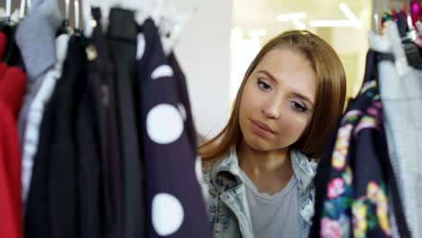 un primer plano de una estudiante comprando ropa, mirando a través de las coloridas prendas en colgadores, tocándolas y moviéndolas. ropa de mujer en primer plano.