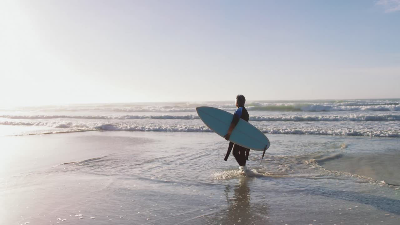 Donna anziana afroamericana che cammina con una tavola da surf in spiaggia