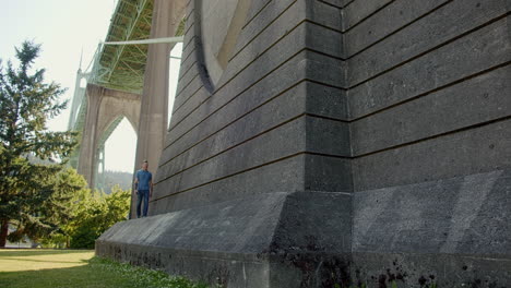 man listening to music on smartphone, walking towards, below bridge, slo mo