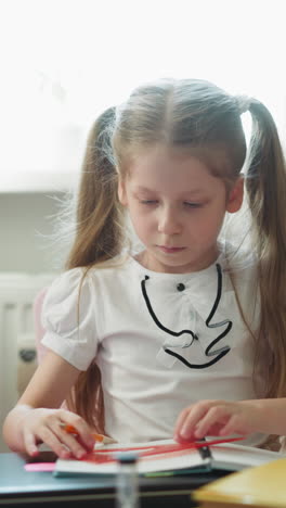 schoolgirl turns pencil and set square sitting at desk. kid sticks out tongue in concentration drawing triangle in paper notepad. pupil studies geometry