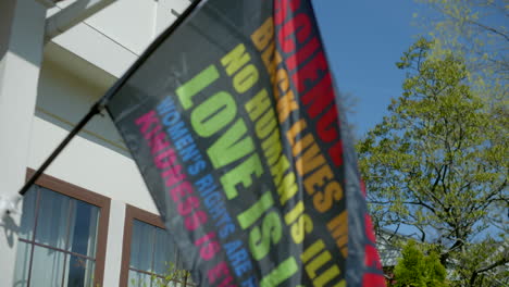 a rainbow equality flag hanging off the front porch of a nice house in the suburbs waves gently in the breeze