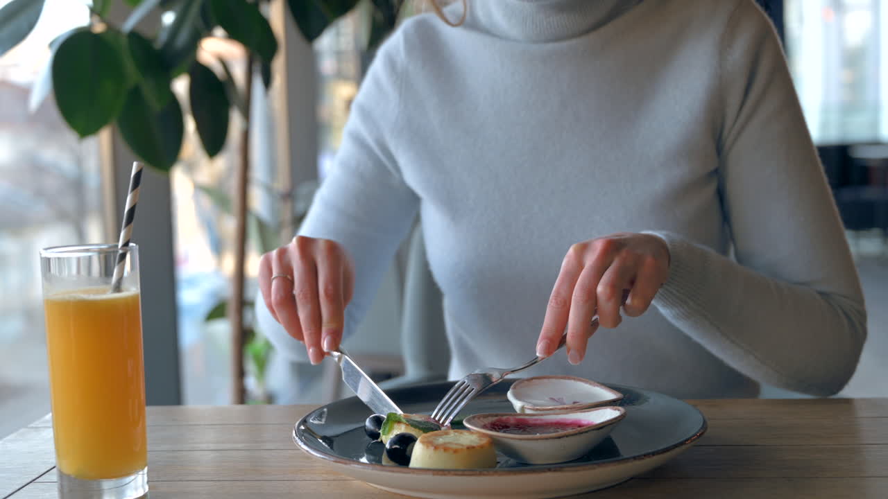 Woman eating cheese pancakes with jam and orange juice at a restaurant
