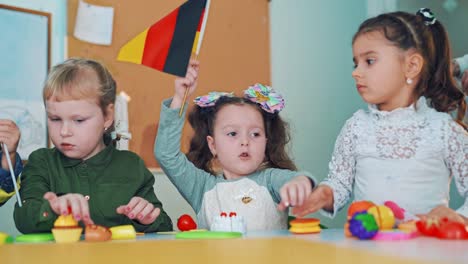 girls sitting with small flags at primary school. one little girl tries to take german flag from other student on the classroom background.