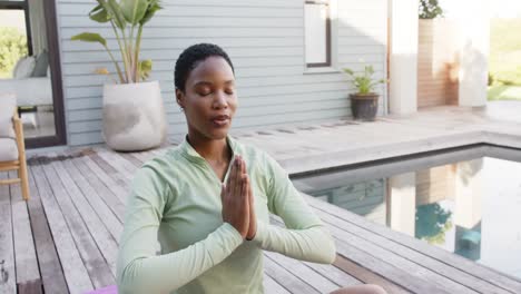 mujer biracial enfocada practicando yoga y meditando en la piscina en el jardín, cámara lenta