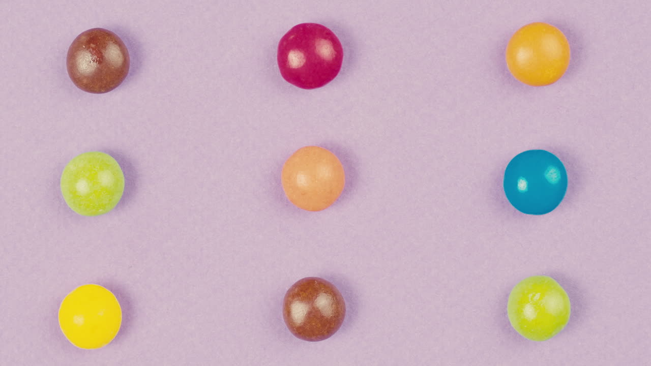 Colorful dragee candies disappear on purple background. Summer bright texture studio shot for store, supermarket, close up top view. Children sweets made of sugar, mix of lollipops, bonbons.