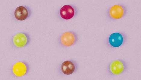 colorful dragee candies disappear on purple background. summer bright texture studio shot for store, supermarket, close up top view. children sweets made of sugar, mix of lollipops, bonbons.