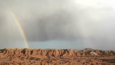 a rainbow fades in the sunlight as it arches over goblin valley state park