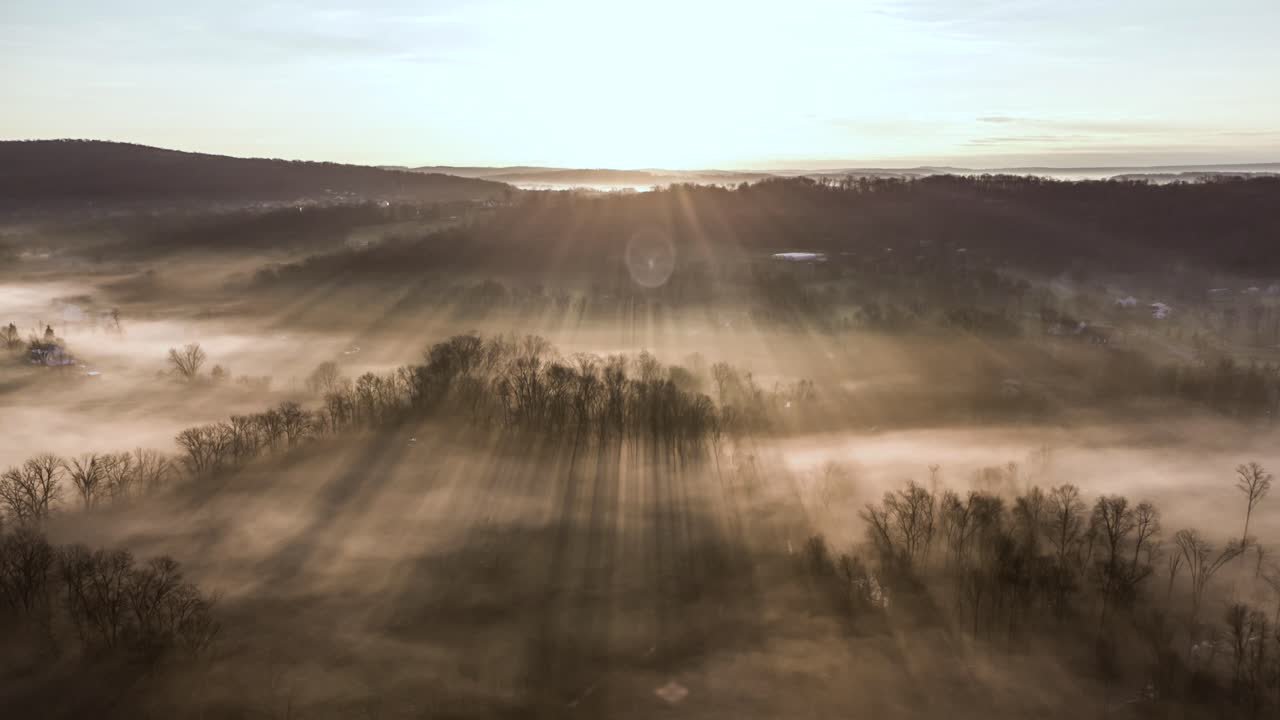 An aerial time-lapse view of the morning fog dispersing with the sun rays shining through the trees