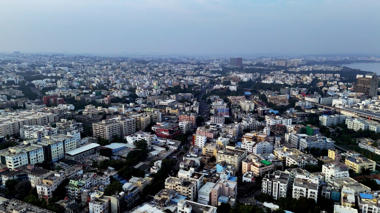Drone shot capturing Khairtabad featuring compact housing clusters, tree-lined areas, and distant commercial towers, emphasizing the scale and layered depth of the urban landscape.