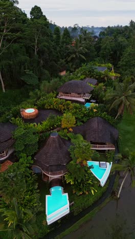 drone footage reveals bamboo villas with pools set in bali’s lush greenery where jungle and ricefields meet creating a luxurious and private tropical paradise from above.
