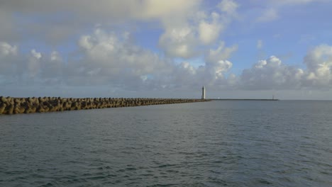 Coastal-view-of-a-pier-stretches-into-the-sea,-ending-with-a-lighthouse-on-the-horizon