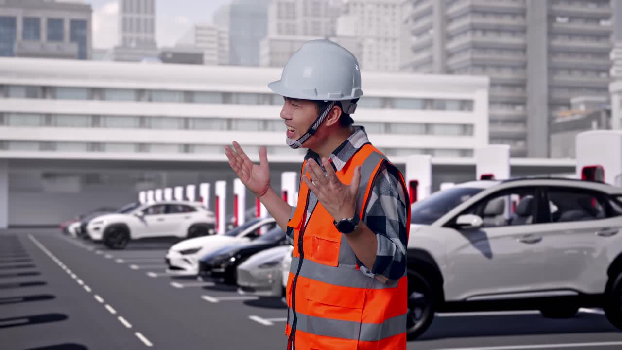 現代の都市型EV充電ステーションで充電中の電気自動車を背景に、安全ヘルメットを着用したアジア人男性エンジニアが横から見た姿で、怪訝そうに「なぜ」と問いかけている様子。