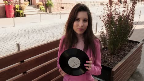 chica moderna y elegante sentada en un banco con un disco en las manos