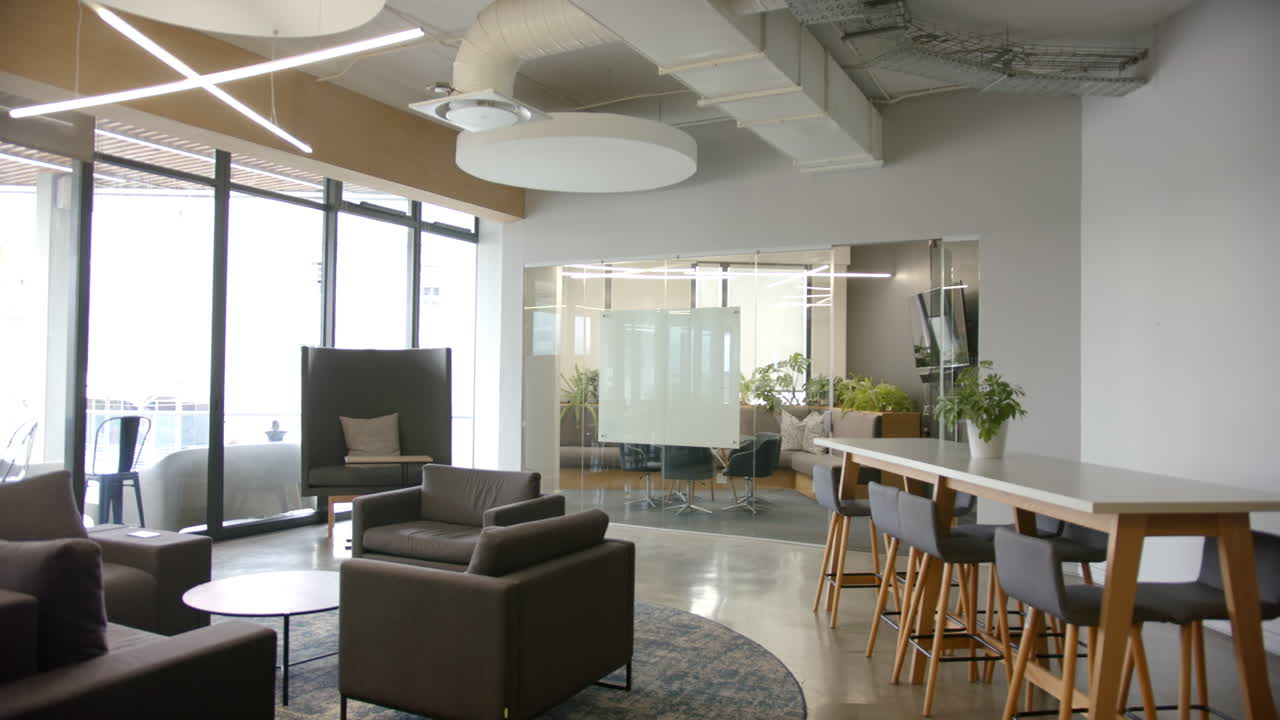 Modern office lounge with comfortable seating, large windows bringing in natural light, copy space