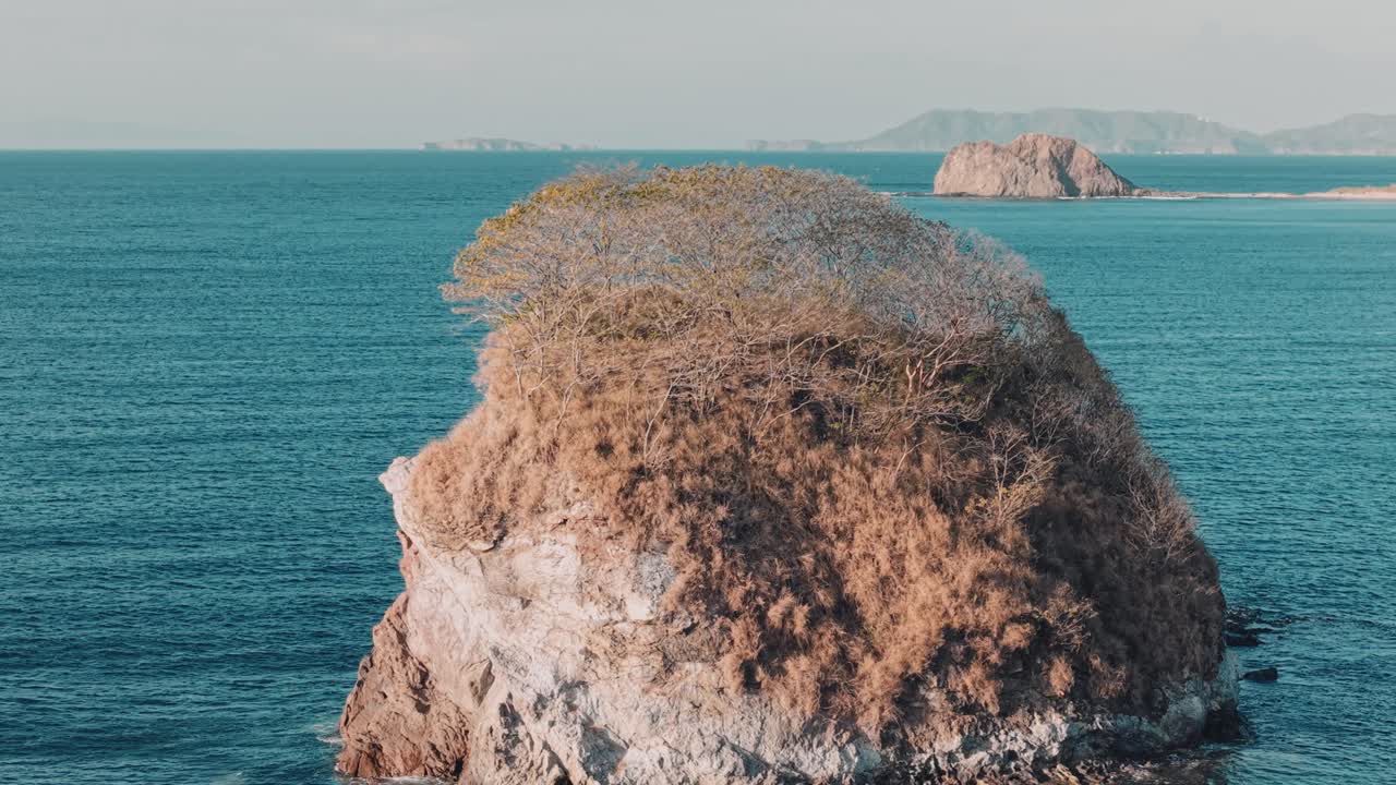 Aerial pan left showing the rocky island with dry vegetation at Bahia Los Piratas beach in Costa Rica