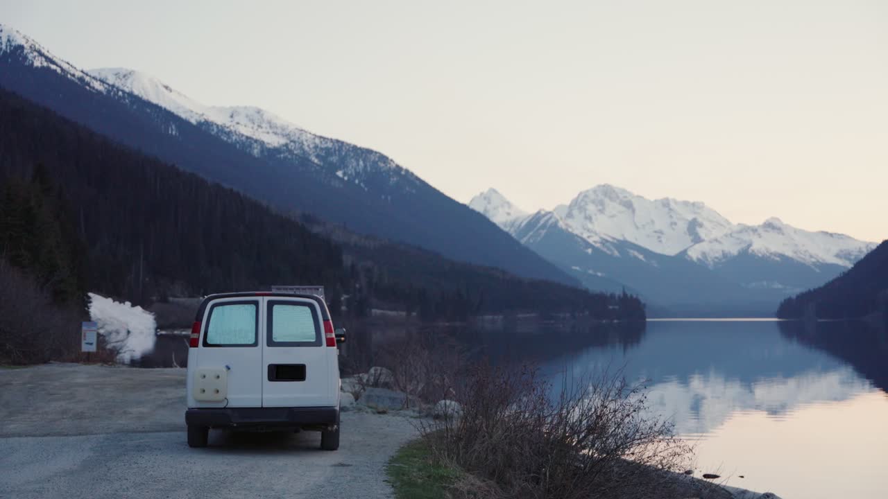 Camper van parked by Duffey Lake reflecting snowy mountains at sunset in British Columbia, Canada