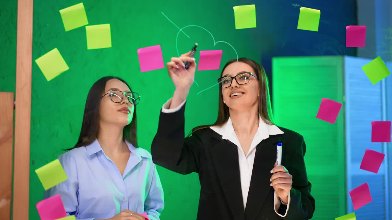 Women brainstorming in office. Two women collaborate creatively using sticky notes on a glass board during a brainstorming session