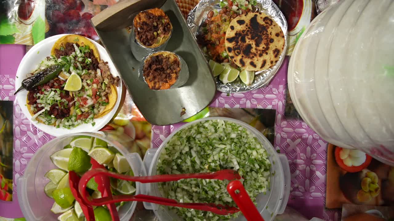 Top-down view of large Mexican burritos surrounded by fresh fillings, sauces, spices, and condiments on a street-style table. Highlights hearty portions, texture, and authentic street cuisine