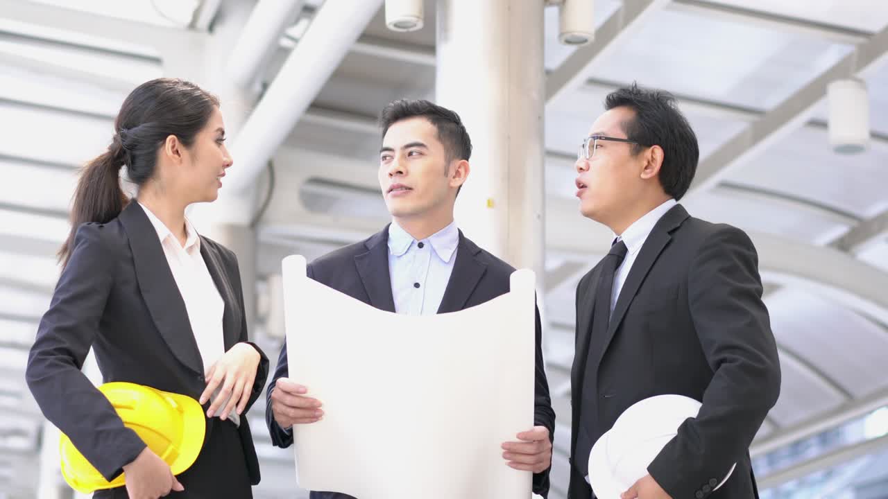 청년 아시아 엔지니어와 사업가들이 블루프린트를 들고 함께 프로젝트를 논의합니다. 프로젝트 관리, 비즈니스 미팅, 전략 및 엔지니어링의 개념.