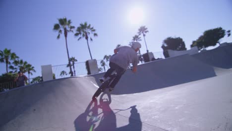 the camera follows a bmx bike rider as he jumps and rides the wall of a skatepark