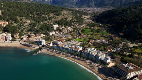 Wunderschöne-Enthüllung-Des-Tropischen-Sandstrandes-Von-Port-Soller,-Mallorca,-Spanien,-An-Heißen-Sommertagen-Mit-Dem-Dorf-Dahinter-In-Der-Ferne-Mit-Kristallklarem-Meer-Und-Unberührtem-Strand