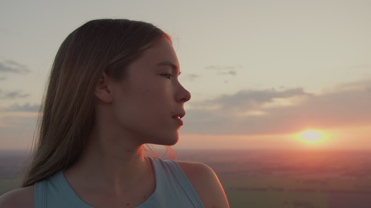 close up profile of young woman gazing toward distant horizon from hot air balloon basket under pastel sunset sky offering serene aerial view over vast open fields with golden glow