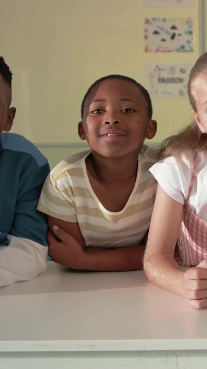 Main student leaning toward classmate for attention then sitting up smiling by white table school
