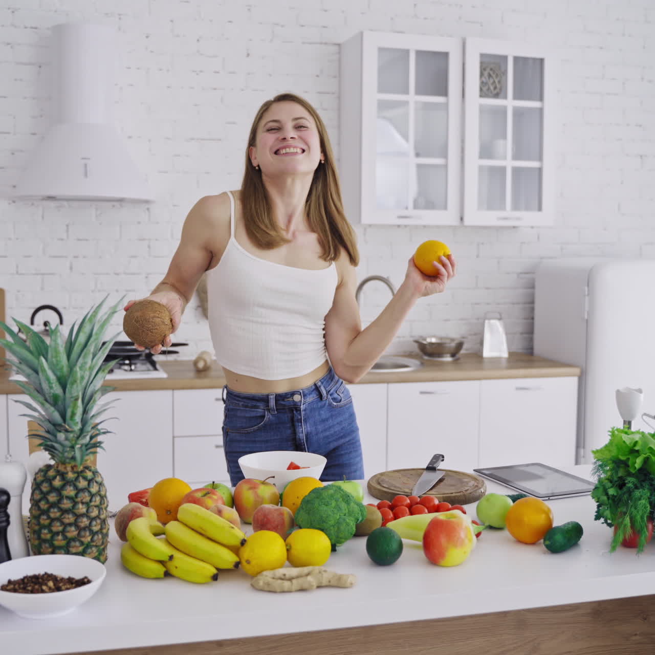 Beautiful slim woman is dancing with fresh fruits in the modern kitchen. Happy woman holding coconut and orange having fun at home. Organic fruit and vegetables. Dieting concept.