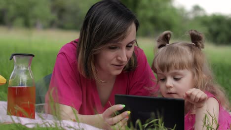 Family-weekend-picnic.-Daughter-child-girl-with-mother-study-lessons-on-tablet.-Distance-education