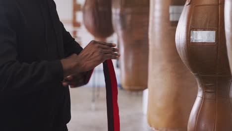 Close-Up-Of-Male-Boxer-Training-In-Gym-Putting-Wraps-On-Hands-Standing-Next-To-Punching-Bag