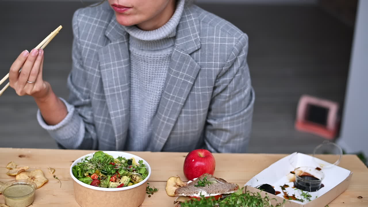 A woman sits at a wooden table savoring a nutritious meal that includes a vibrant salad, fruit, and various condiments. The cozy atmosphere creates a perfect lunchtime vibe