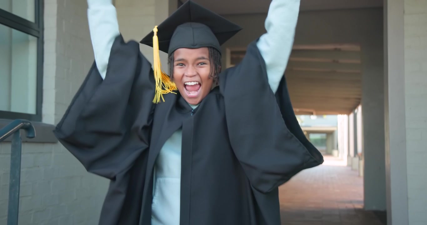 African American teen in gown and cap holding rolled diploma and celebrating graduation in corridor